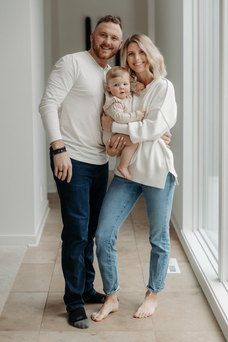 Ben and Zoie, founders of WOODCHUCK USA, smiling and holding their young child in a sunlit home.